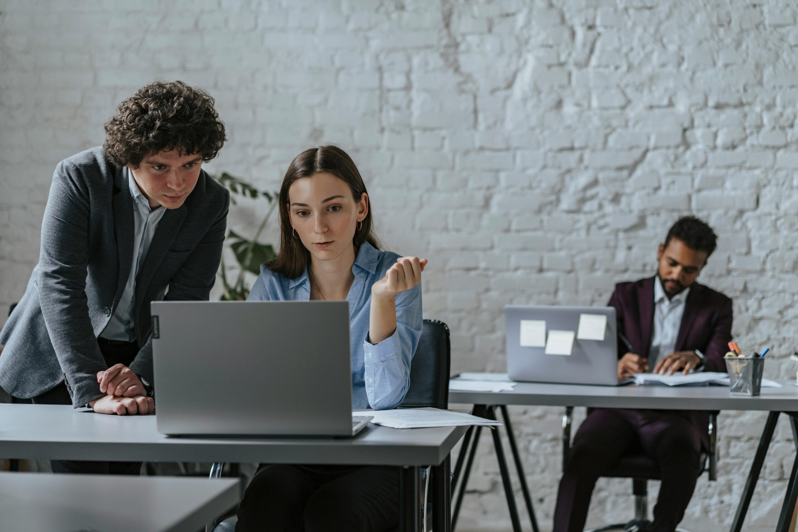Three professionals working together in a contemporary office space, focused on a laptop task.